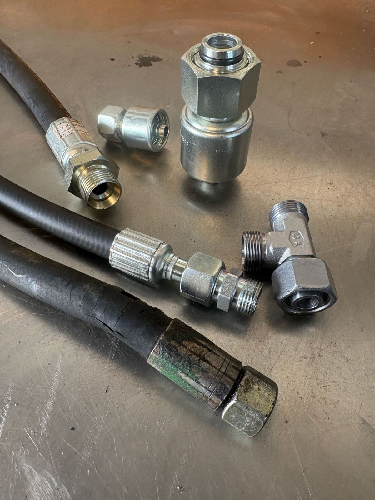 Hydraulikschläuche mit neuen Pressarmaturen, T-Verschraubung und einem alten, rissigen Schlauch auf der Werkbank